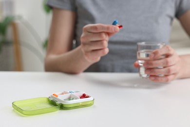 Photo of Woman with pills, organizer and glass of water at white table, selective focus