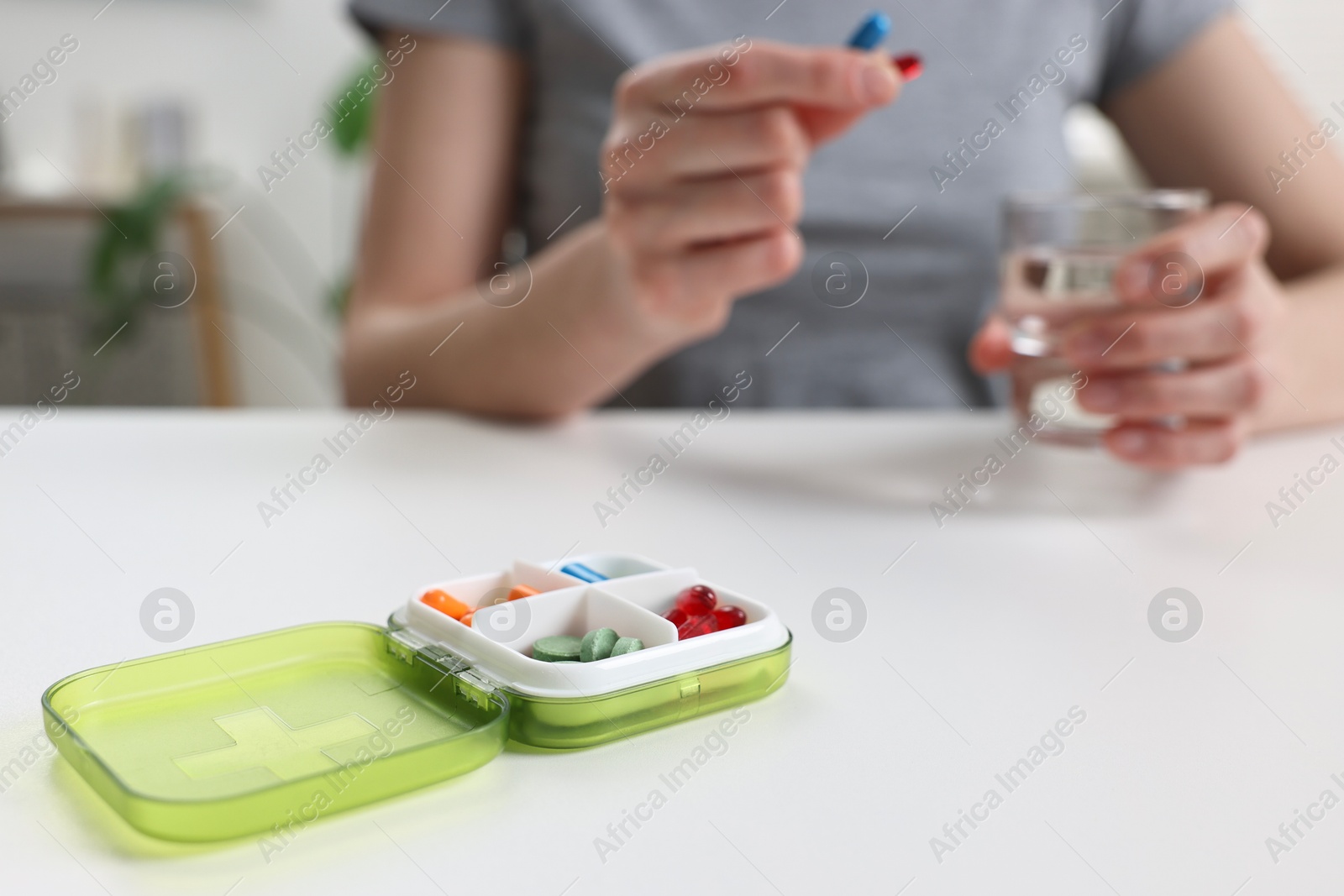 Photo of Woman with pills, organizer and glass of water at white table, selective focus