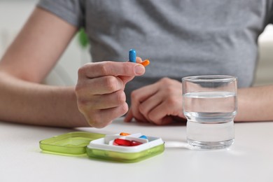 Photo of Woman with pills, organizer and glass of water at white table, closeup