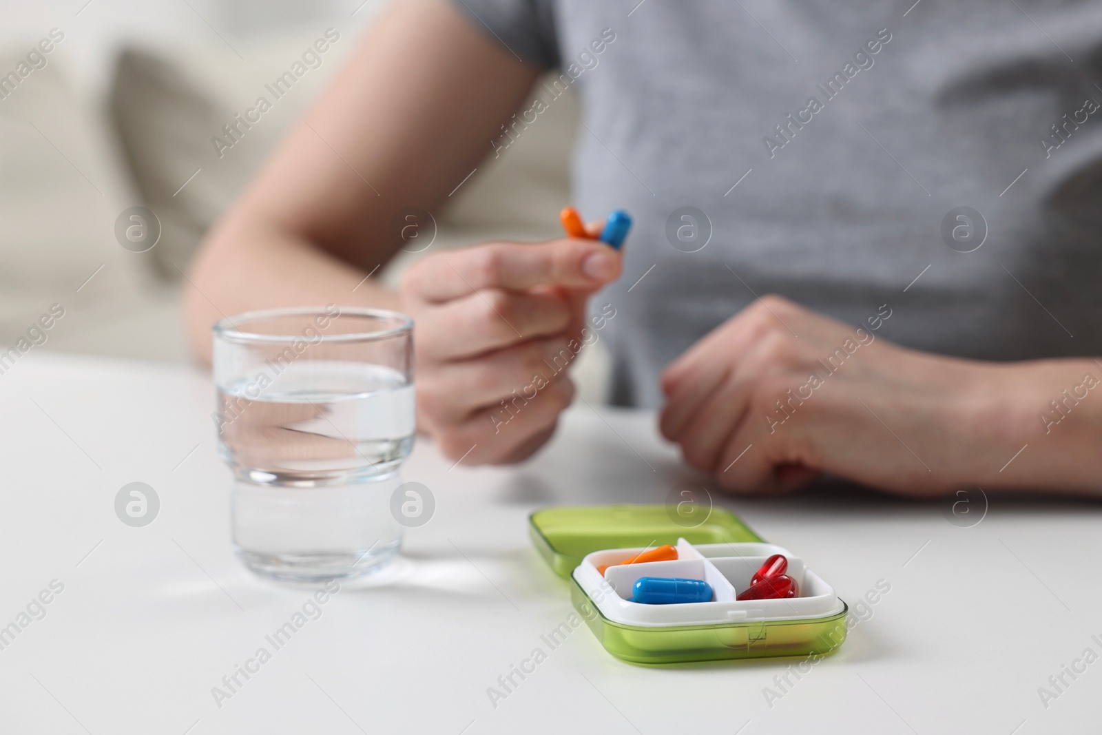 Photo of Woman with pills, organizer and glass of water at white table, selective focus