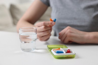 Woman with pills, organizer and glass of water at white table, selective focus