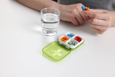 Photo of Woman with pills, organizer and glass of water at white table, closeup