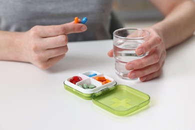 Woman with pills, organizer and glass of water at white table, closeup