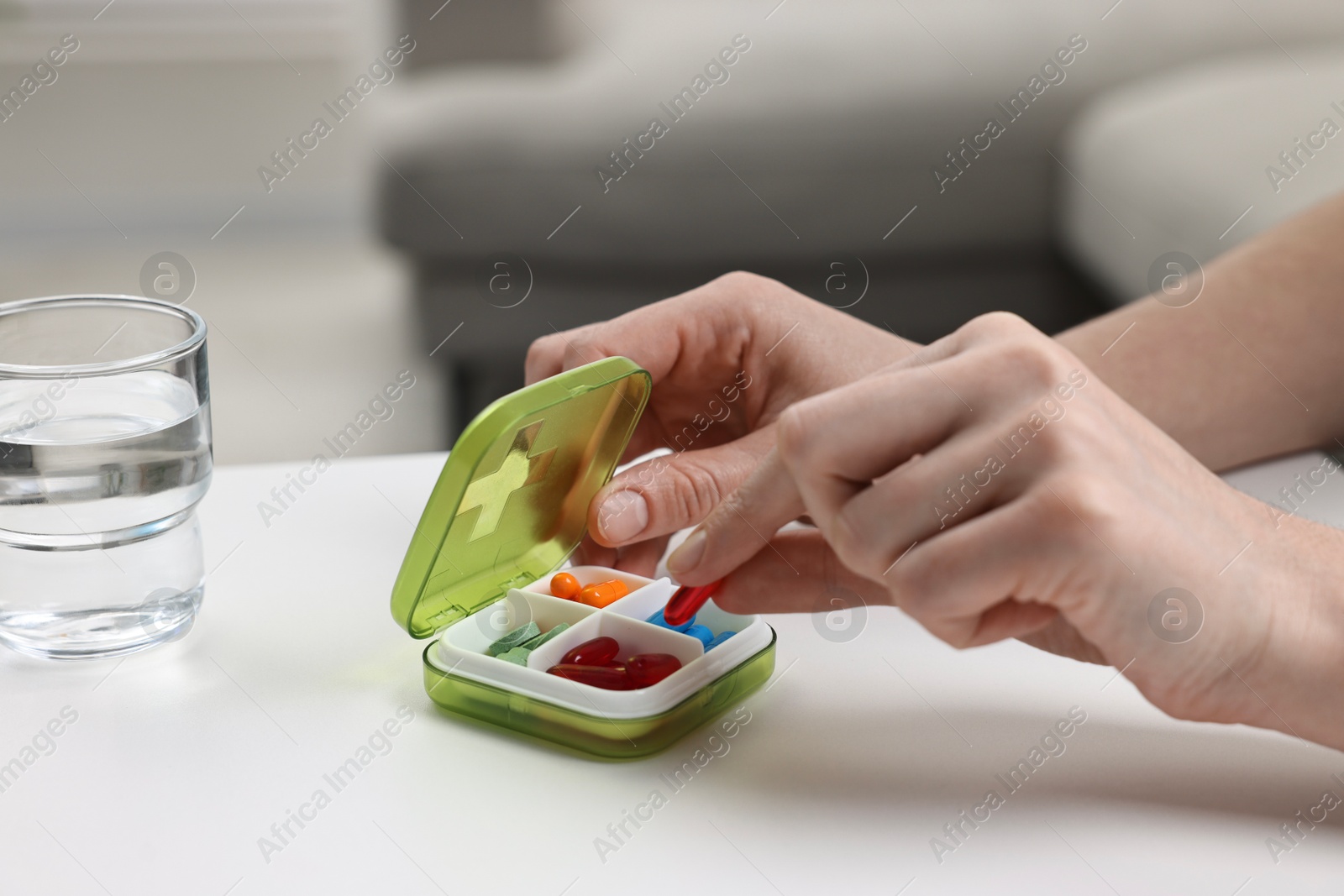 Photo of Woman with pills, organizer and glass of water at white table, closeup