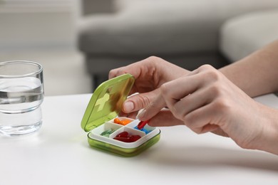 Photo of Woman with pills, organizer and glass of water at white table, closeup