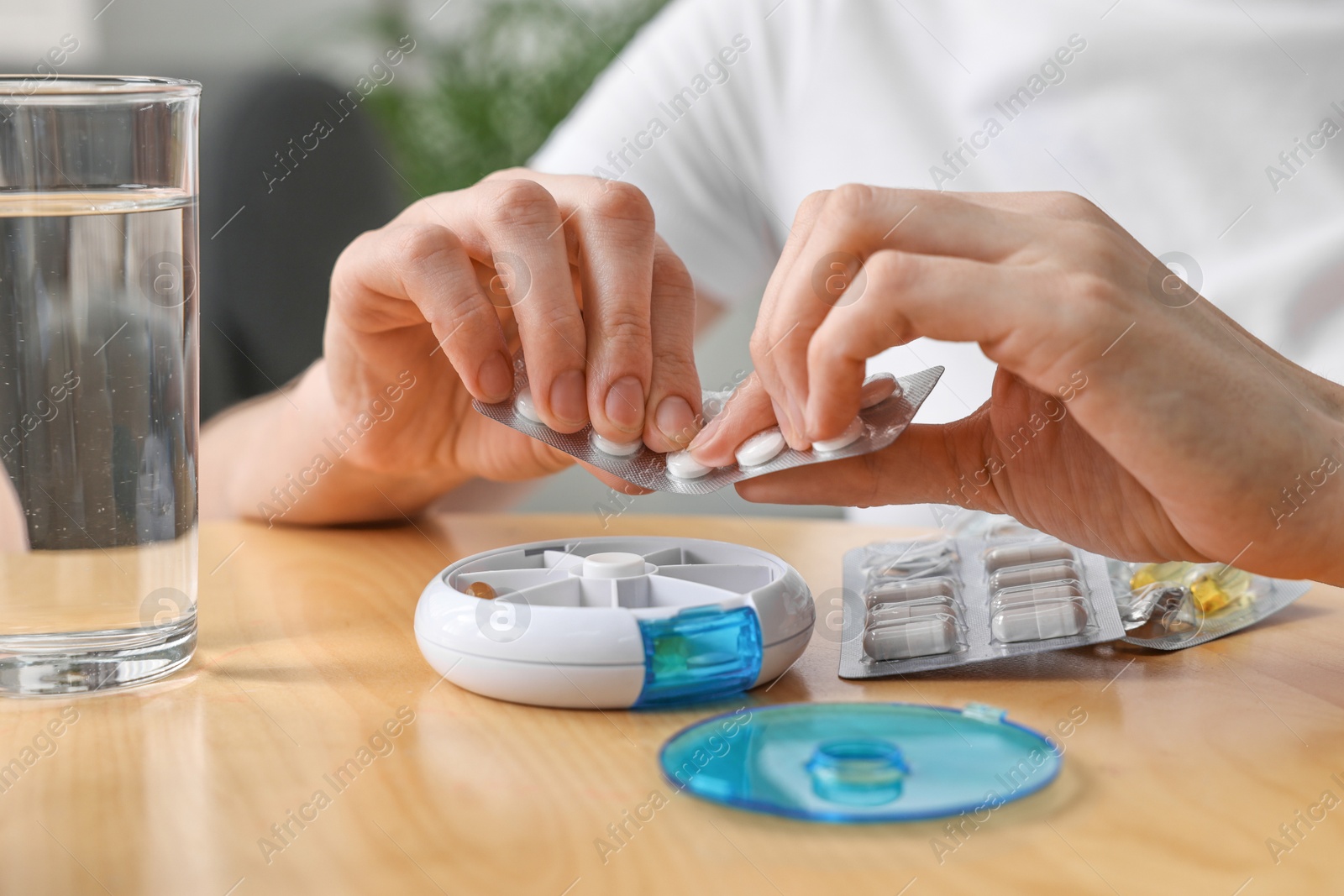 Photo of Woman with pills, organizer and glass of water at light wooden table, closeup