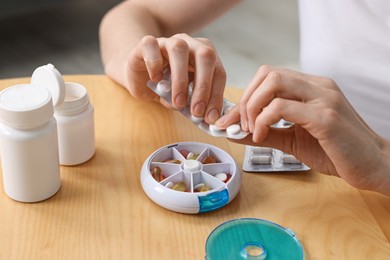 Photo of Woman with pills and organizer at light wooden table, closeup