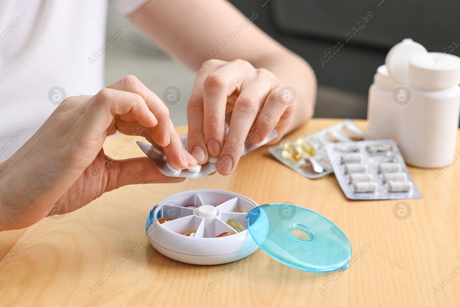 Photo of Woman with pills and organizer at light wooden table, closeup