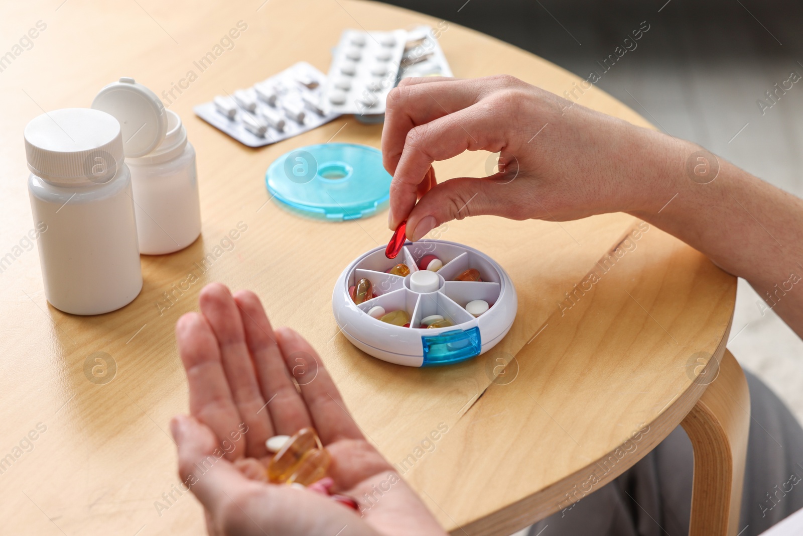 Photo of Woman with pills and organizer at light wooden table, closeup