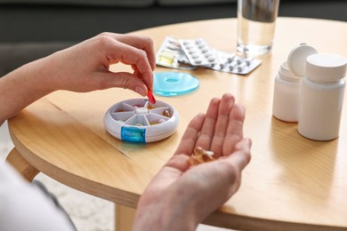 Photo of Woman with pills, organizer and glass of water at light wooden table, closeup