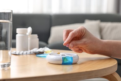 Photo of Woman with pills, organizer and glass of water at light wooden table, closeup