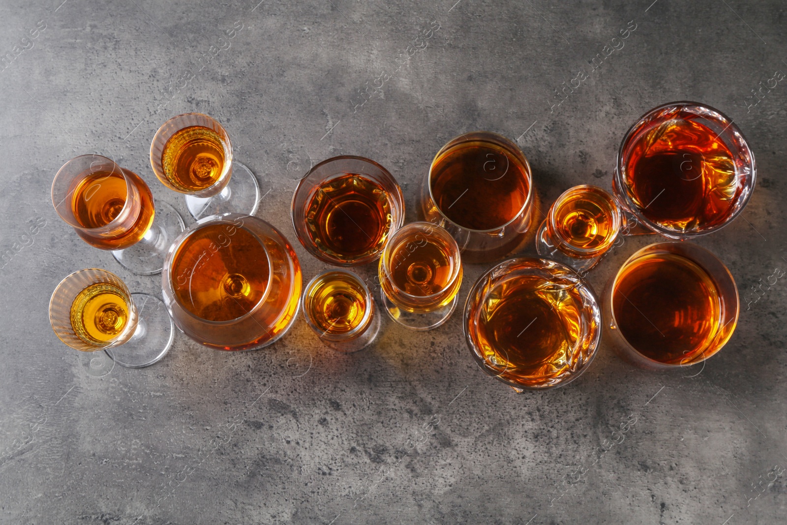 Photo of Different delicious liqueurs in glasses on grey table, flat lay