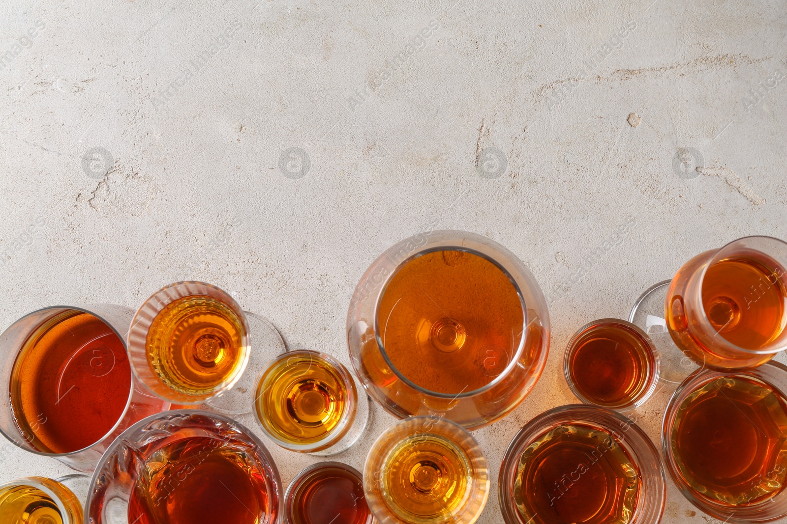 Photo of Different delicious liqueurs in glasses on light grey table, flat lay. Space for text