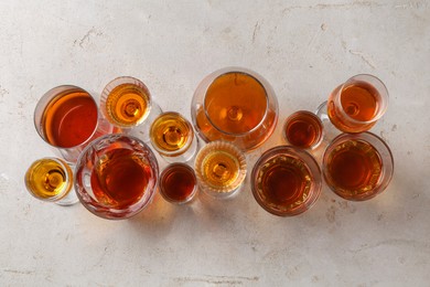 Different delicious liqueurs in glasses on light grey table, flat lay