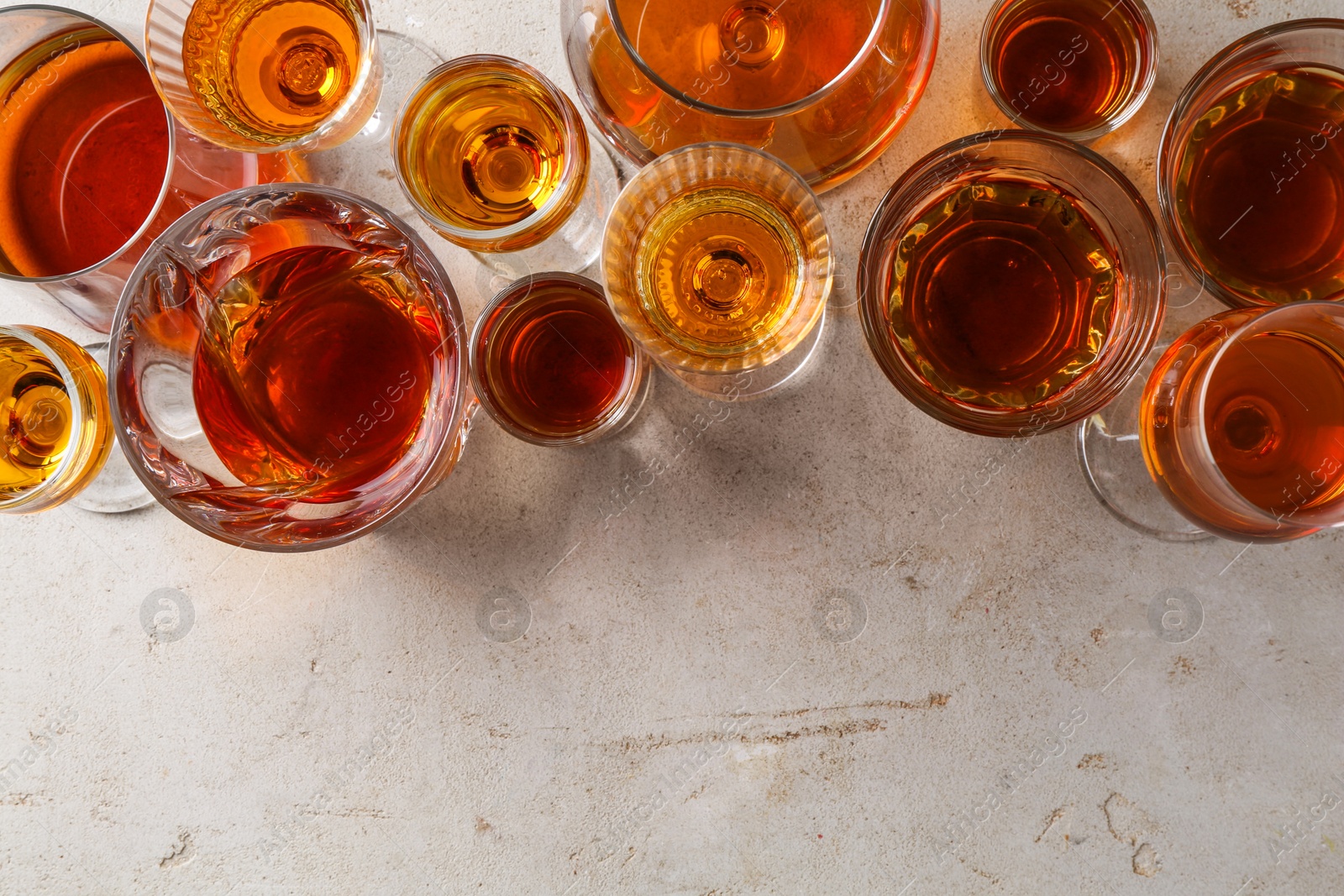 Photo of Different delicious liqueurs in glasses on light grey table, flat lay. Space for text