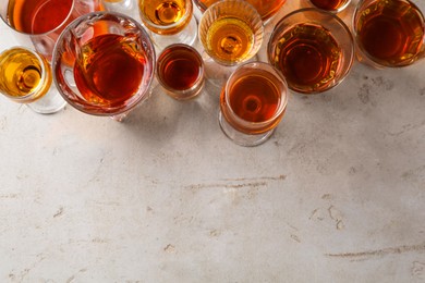 Photo of Different delicious liqueurs in glasses on light grey table, flat lay. Space for text