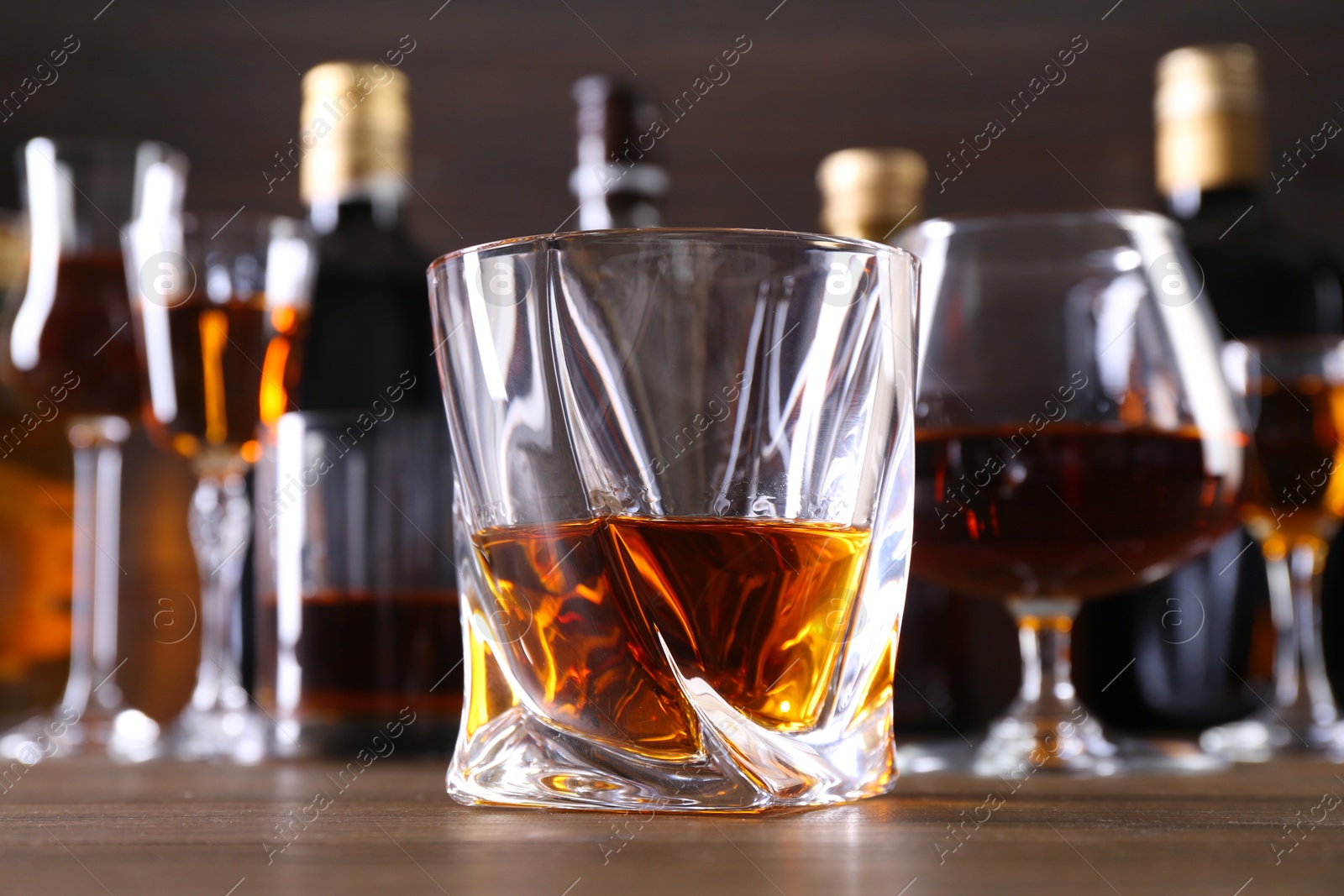 Photo of Different delicious liqueurs in glasses and bottles on wooden table, closeup