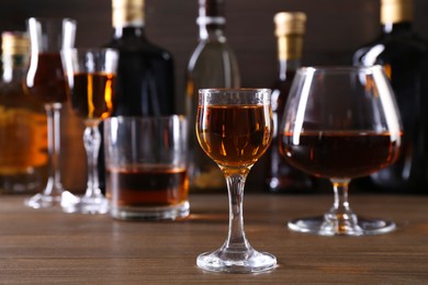 Photo of Different delicious liqueurs in glasses and bottles on wooden table