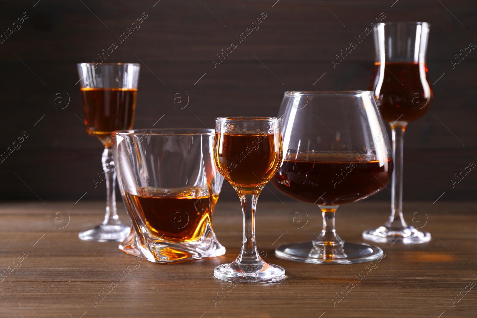 Photo of Different delicious liqueurs in glasses on wooden table