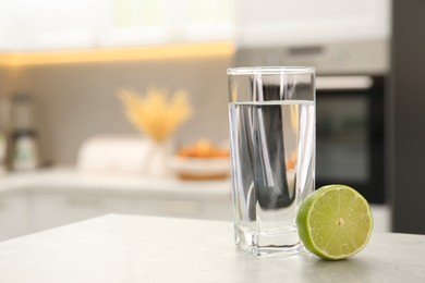 Photo of Filtered water in glass and lime on light table in kitchen, closeup. Space for text