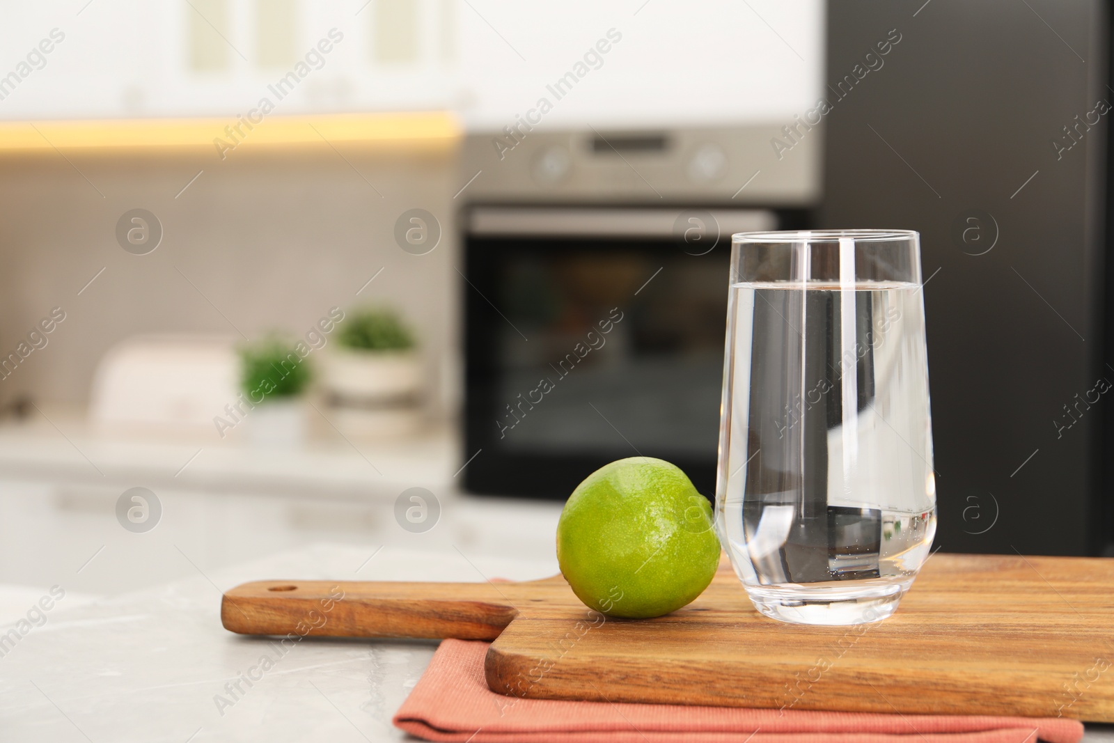 Photo of Filtered water in glass and lime on light marble table in kitchen, closeup. Space for text