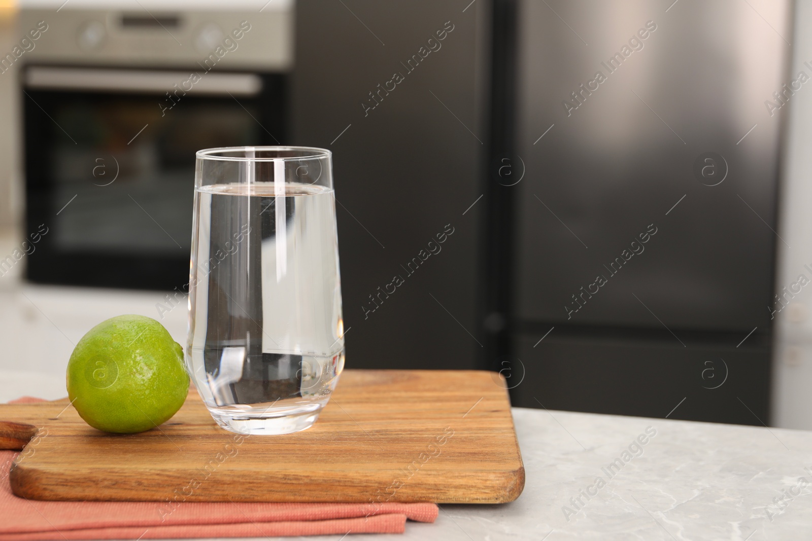 Photo of Filtered water in glass and lime on light marble table in kitchen, closeup. Space for text