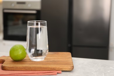 Photo of Filtered water in glass and lime on light marble table in kitchen, closeup. Space for text