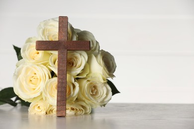 Photo of Bible, cross and roses on light wooden table against white background, space for text. Religion of Christianity