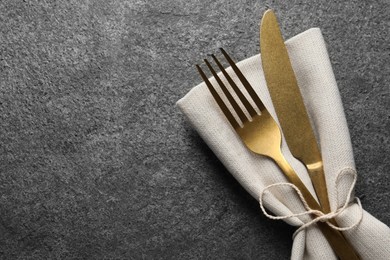 Photo of Stylish golden cutlery and napkin on grey table, top view. Space for text