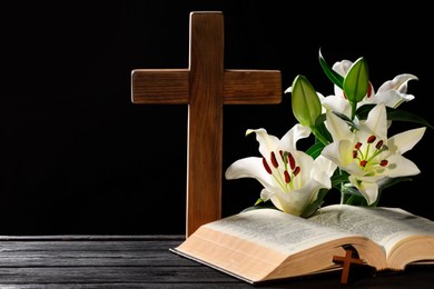 Bible, crosses and lilies on dark gray wooden table against black background, space for text. Religion of Christianity