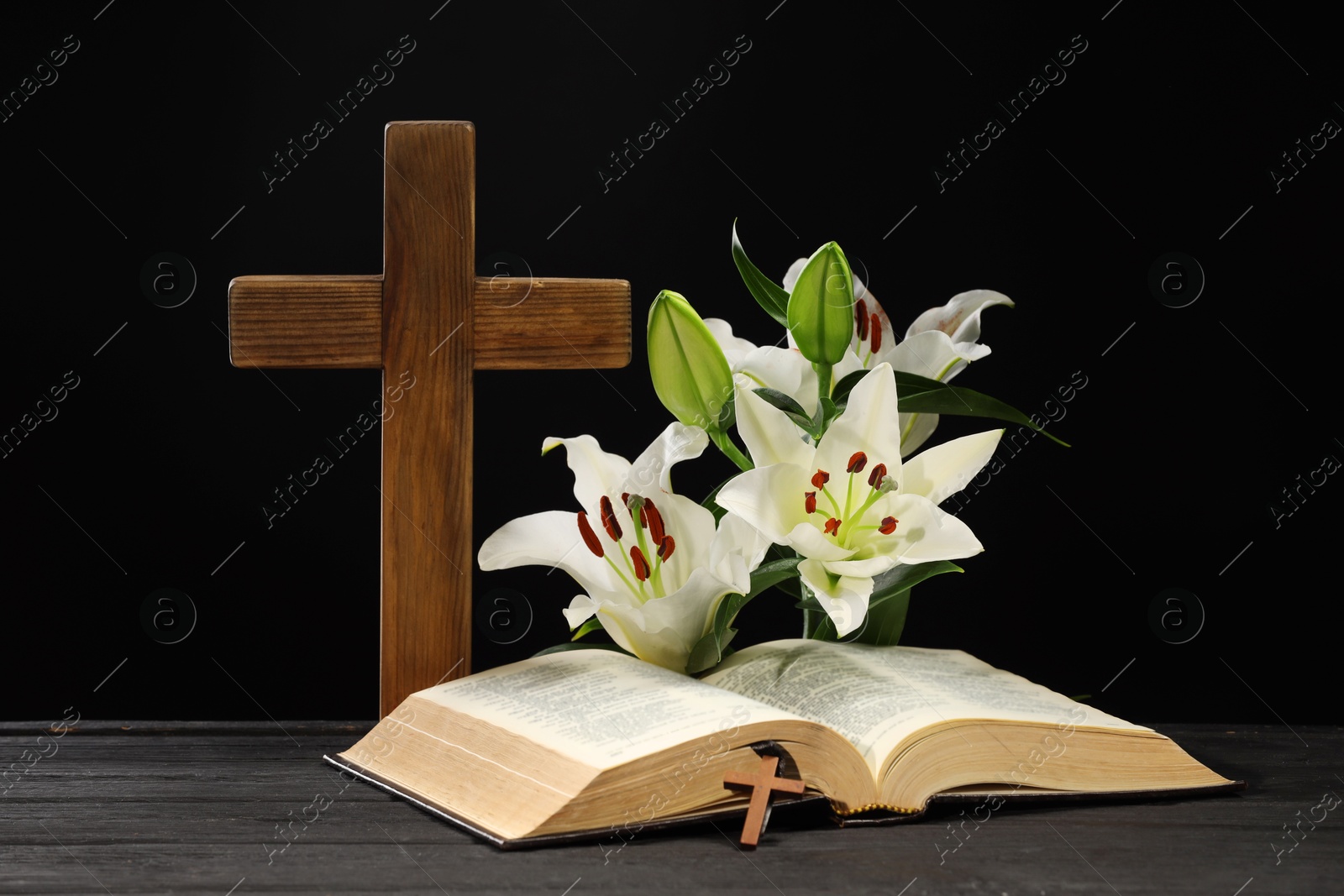 Photo of Bible, crosses and lilies on dark gray wooden table against black background. Religion of Christianity