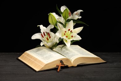Bible, cross and lilies on dark gray wooden table against black background. Religion of Christianity