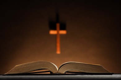 Bible and cross on brown wall, selective focus. Religion of Christianity