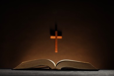 Bible and cross on brown wall, selective focus. Religion of Christianity