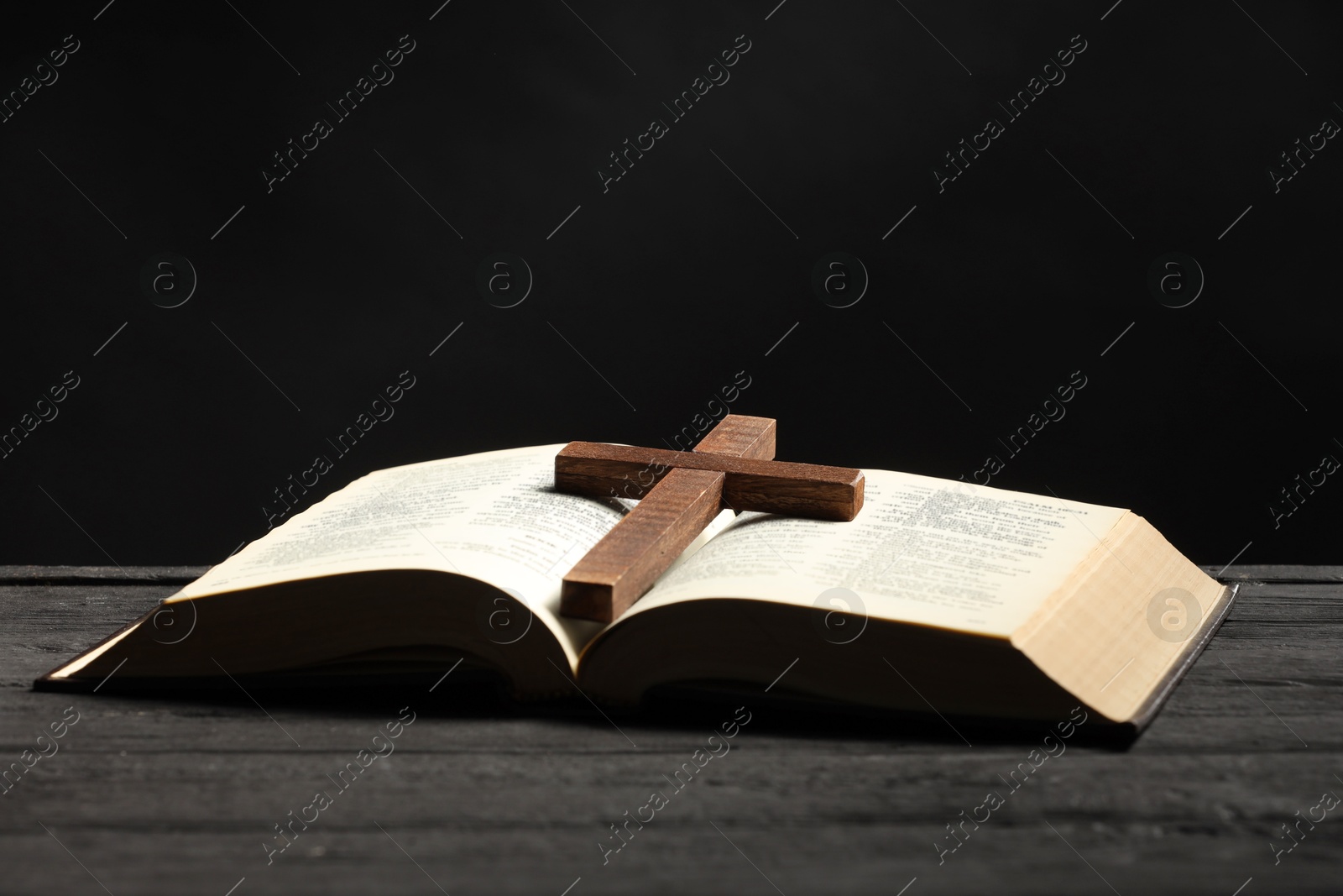 Photo of Bible and cross on gray wooden table against dark background, space for text. Religion of Christianity