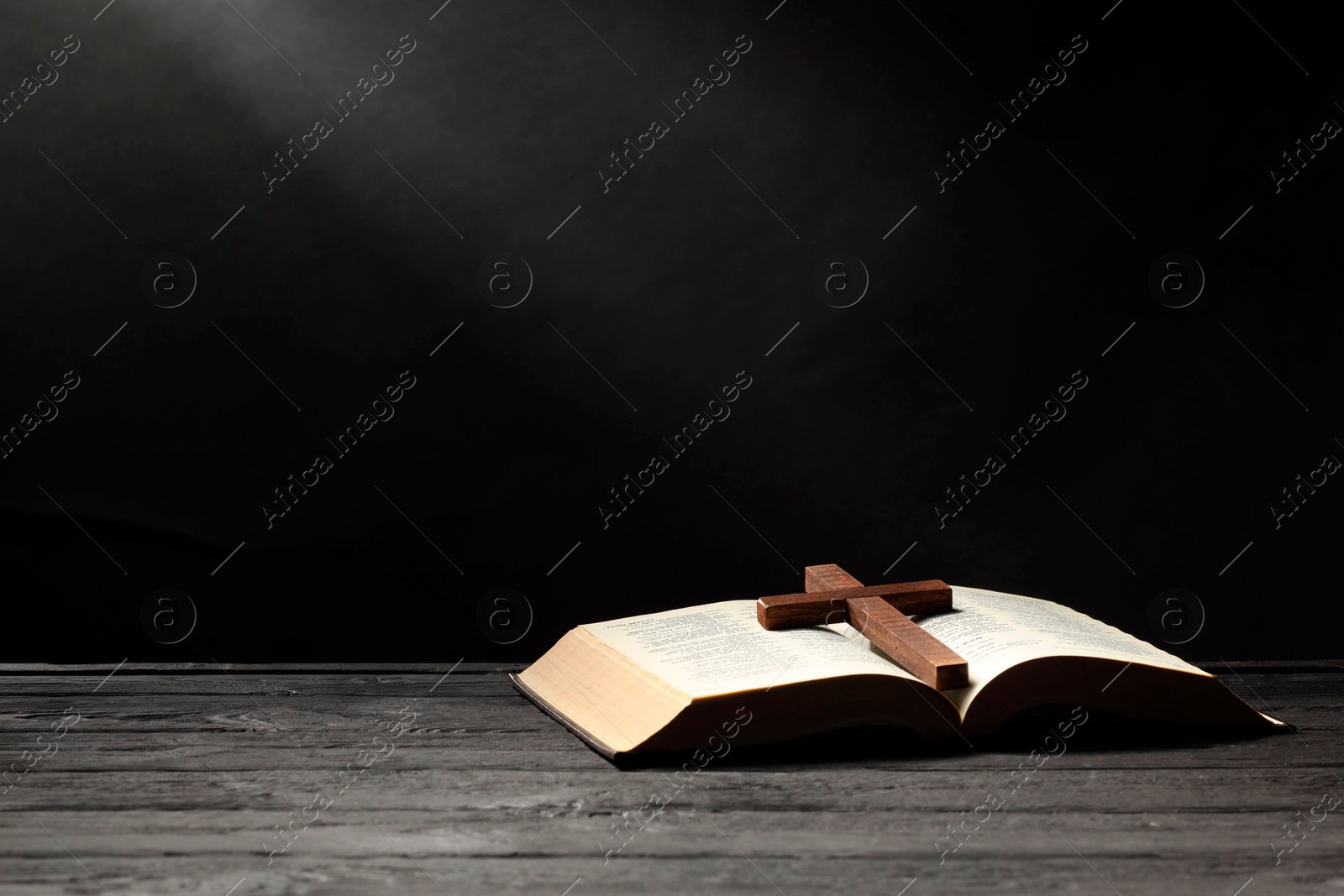 Photo of Bible and cross on gray wooden table against dark background, space for text. Religion of Christianity
