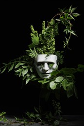 Photo of Theatrical performance. Plastic mask and floral decor on table against black background