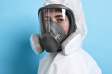 Worker in respirator and protective suit on light blue background