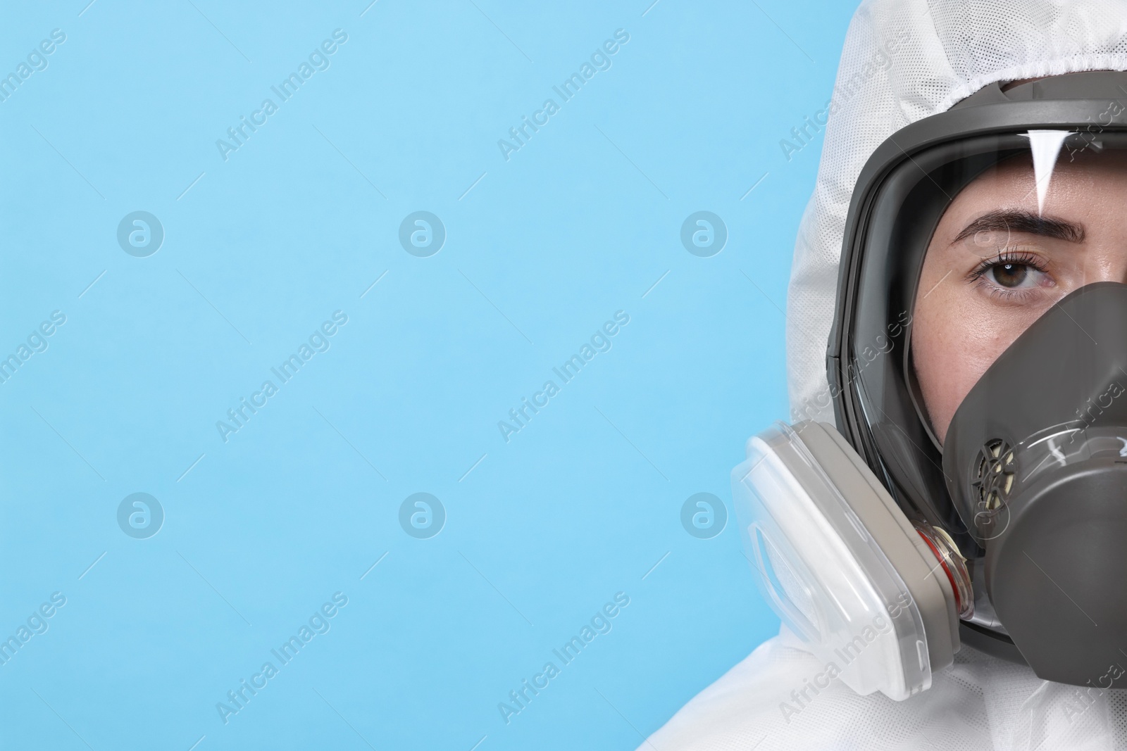 Photo of Worker in respirator and protective suit on light blue background, space for text