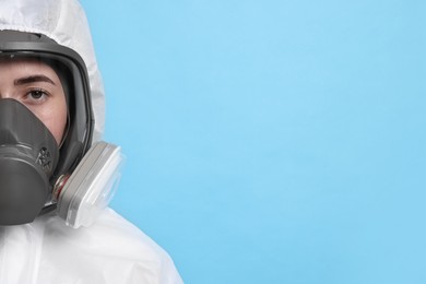 Worker in respirator and protective suit on light blue background, space for text