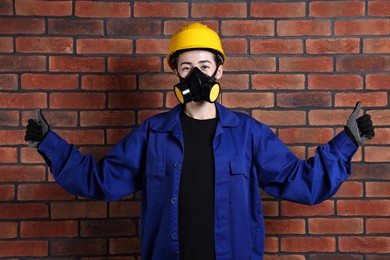 Photo of Worker in respirator and helmet showing thumbs up near brick wall