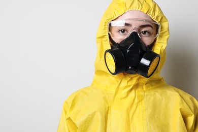 Worker in respirator, protective suit and glasses on grey background, space for text