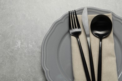 Stylish cutlery, napkin and plate on grey table, top view. Space for text