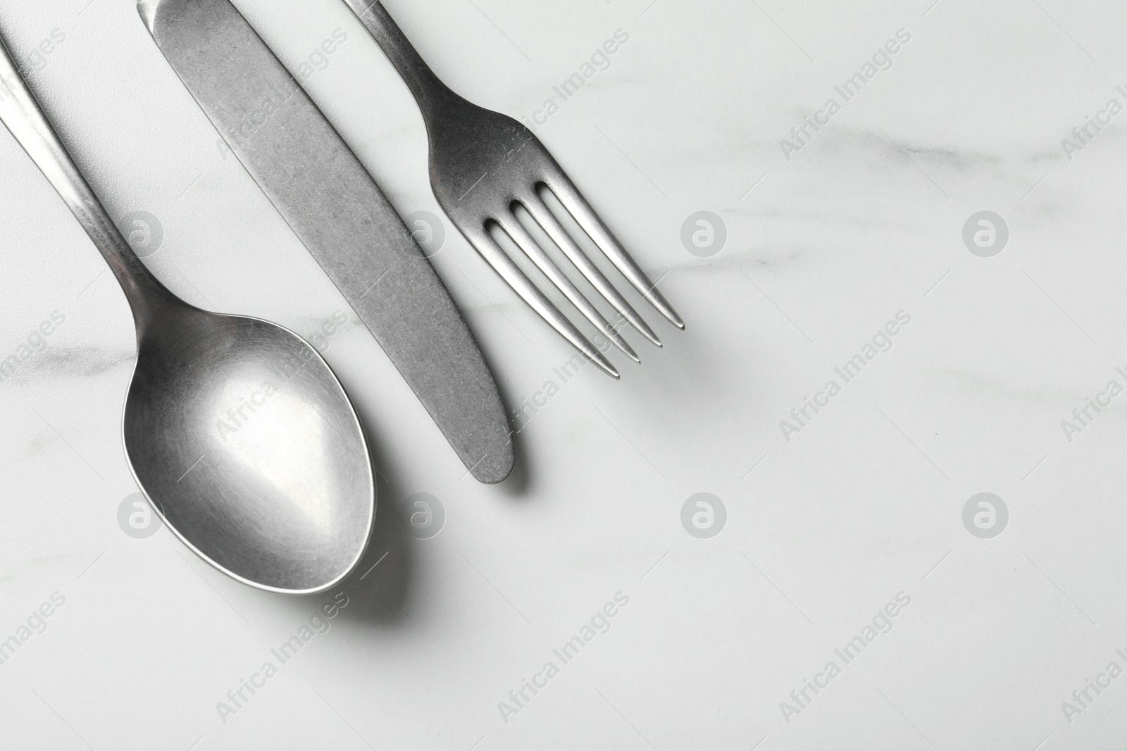 Photo of Stylish silver cutlery set on white marble table, flat lay. Space for text