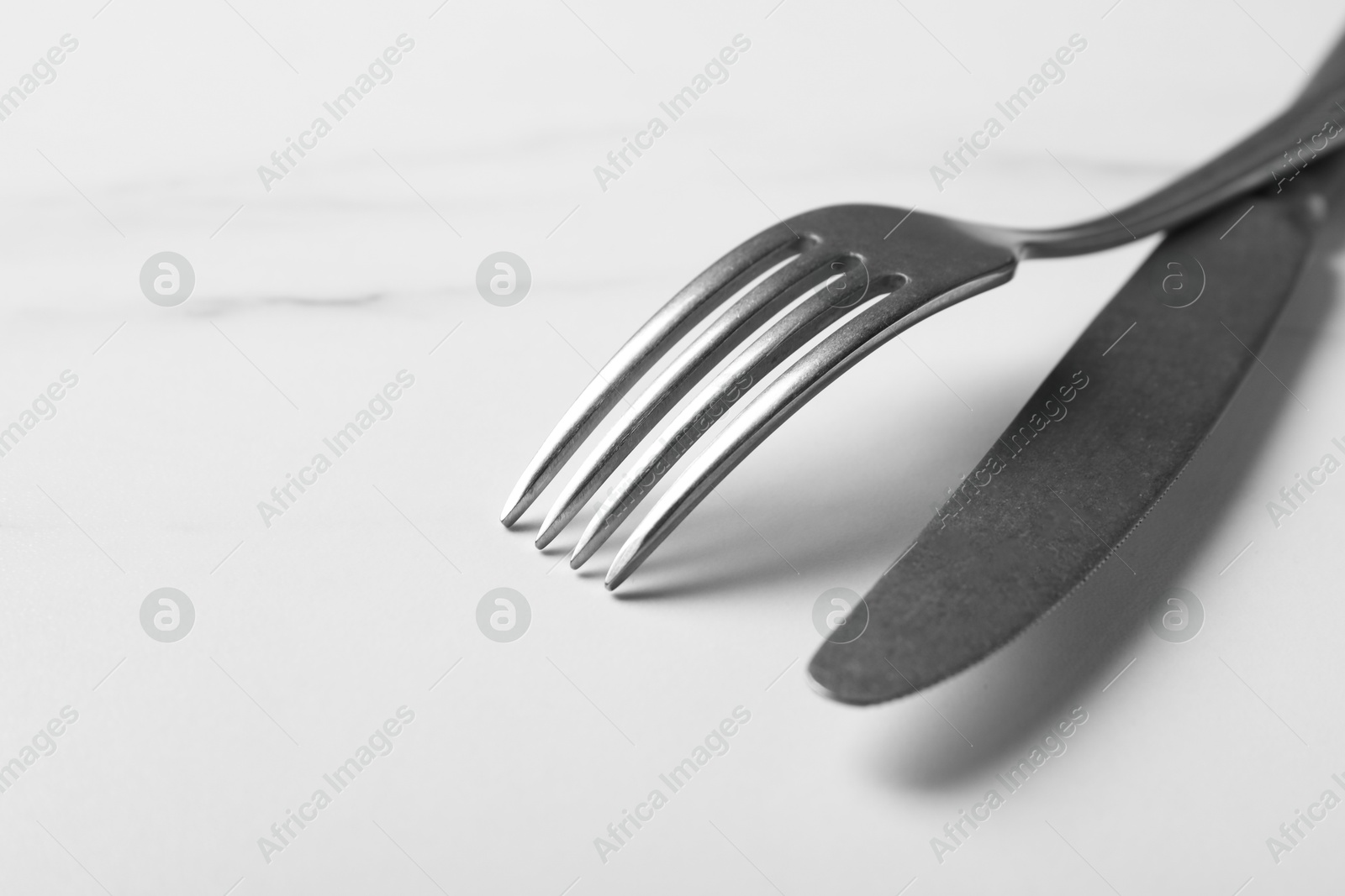 Photo of Stylish cutlery. Silver knife and fork on white marble table, closeup. Space for text