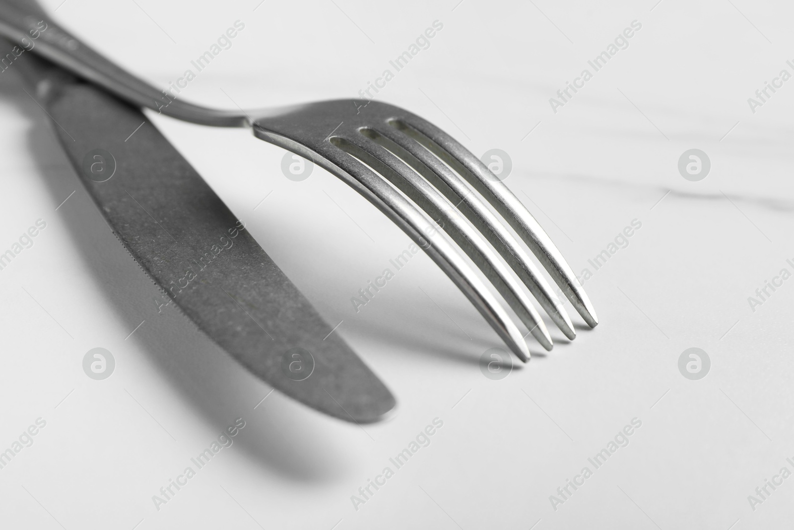 Photo of Stylish cutlery. Silver knife and fork on white marble table, closeup