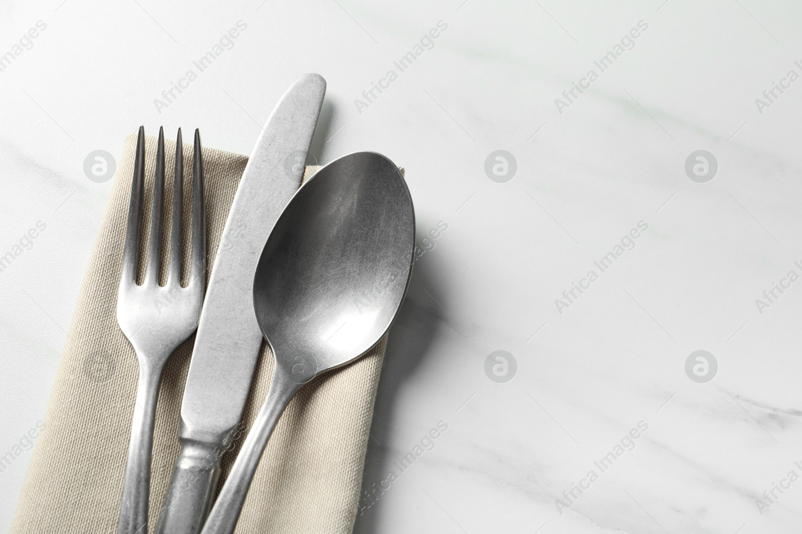 Photo of Set of stylish cutlery and napkin on white marble table, top view. Space for text