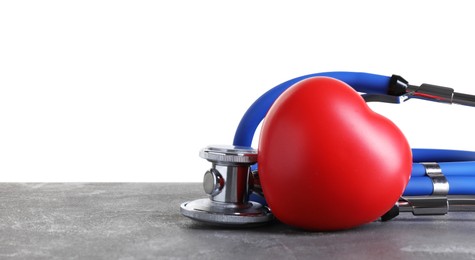 Stethoscope and red heart on grey table against white background, space for text