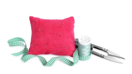 Photo of Pink pincushion, sewing needles, spool of thread, ribbon and cutter isolated on white