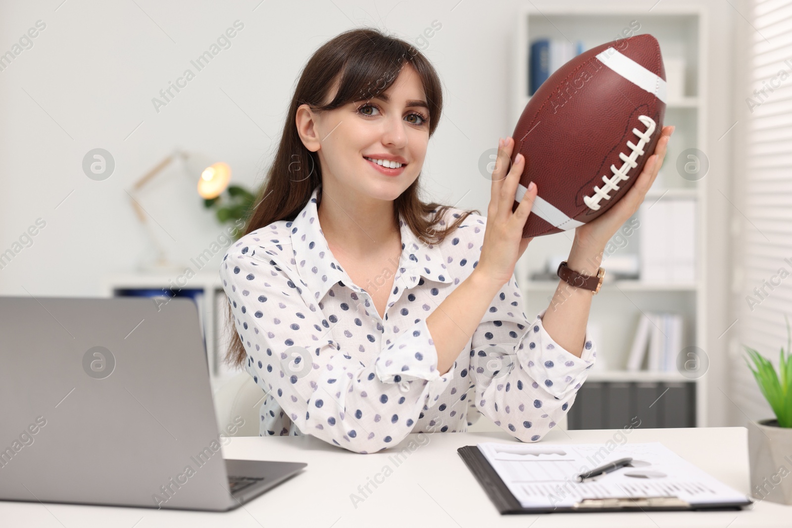 Photo of Smiling employee with american football ball at table in office